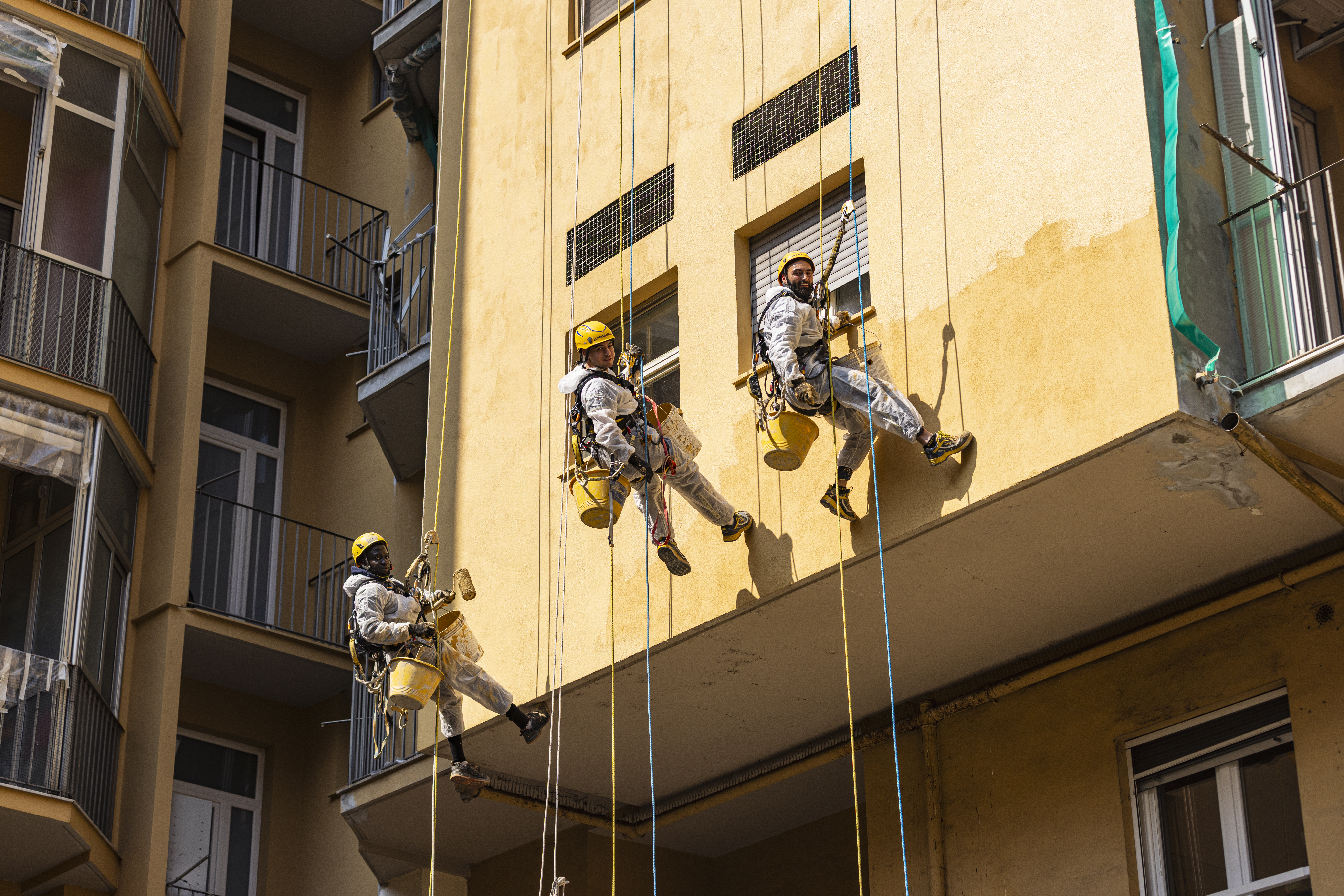operai acrobatica su fune davanti a palazzo giallo durante un'operazione di ripristino intonaco