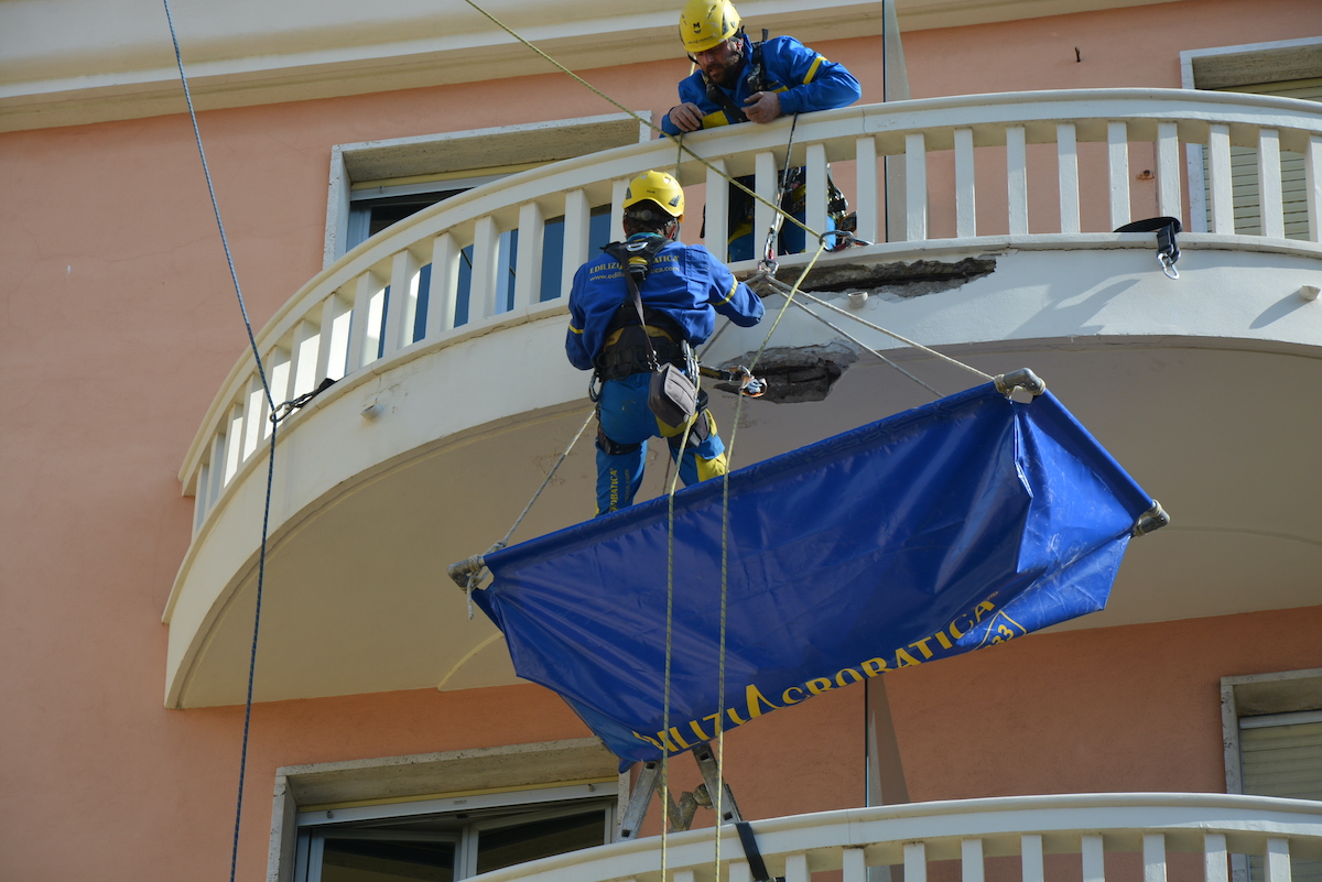 Impermeabilizzare i terrazzi con Acrobatica. Foto di operaio su fune durante un lavoro su balcone con collega. 